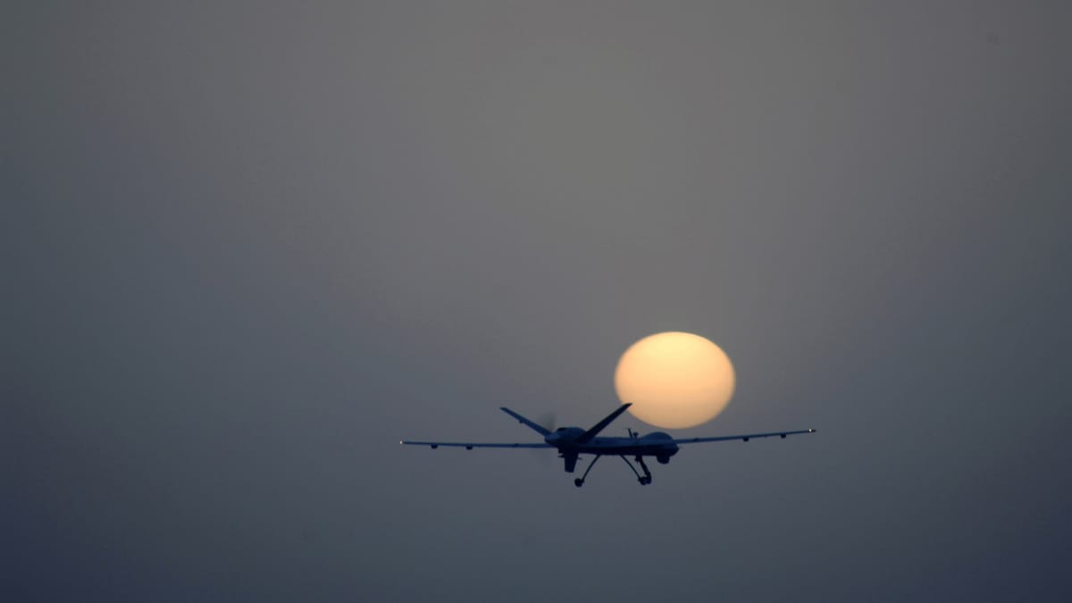 Drone MQ-9 Reaper voando em silhueta contra a lua durante o pôr do sol.