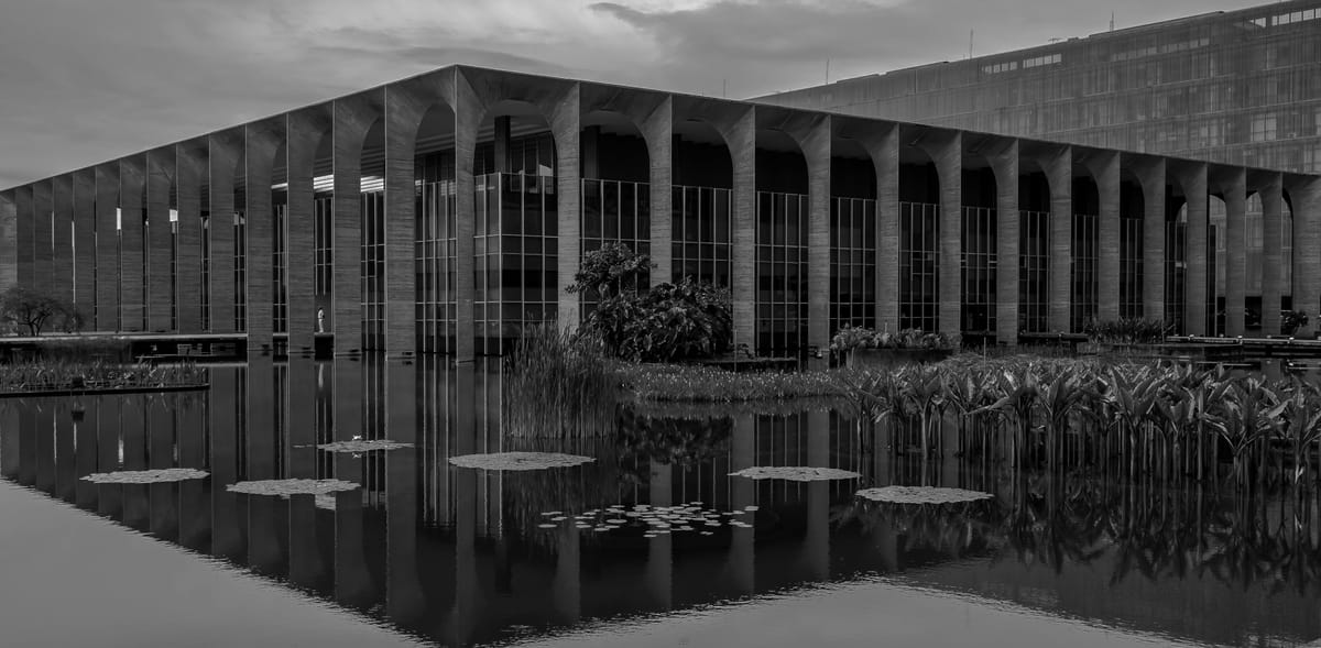 Fotografia em preto e branco do Palácio do Itamaraty em Brasília, refletido na água.